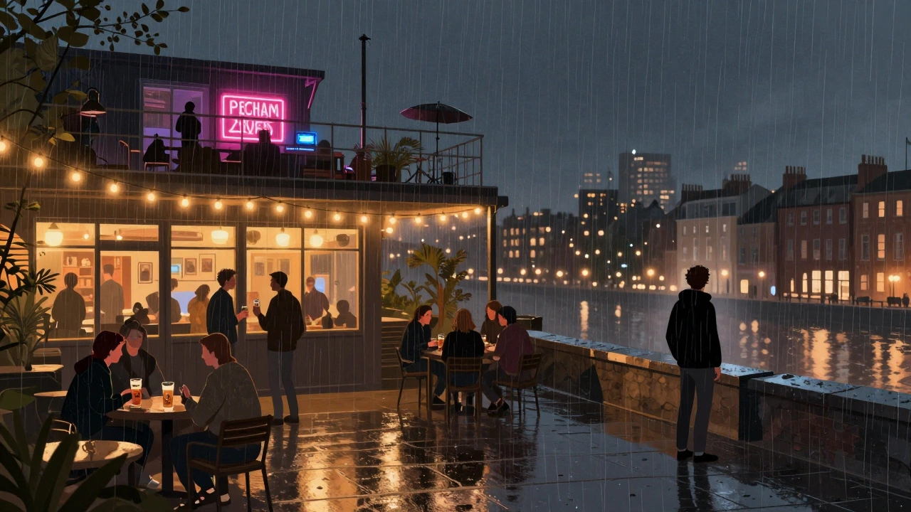 Rooftop terrace at Peckham Levels at night, string lights, people with drinks, city lights in the distance.