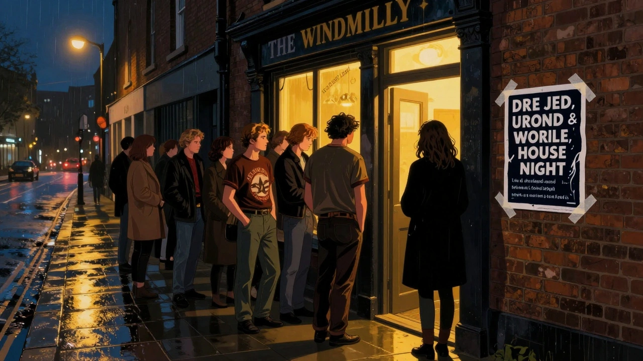 Small group waiting outside The Windmill in Brixton at night, warm light and rain-slicked pavement.