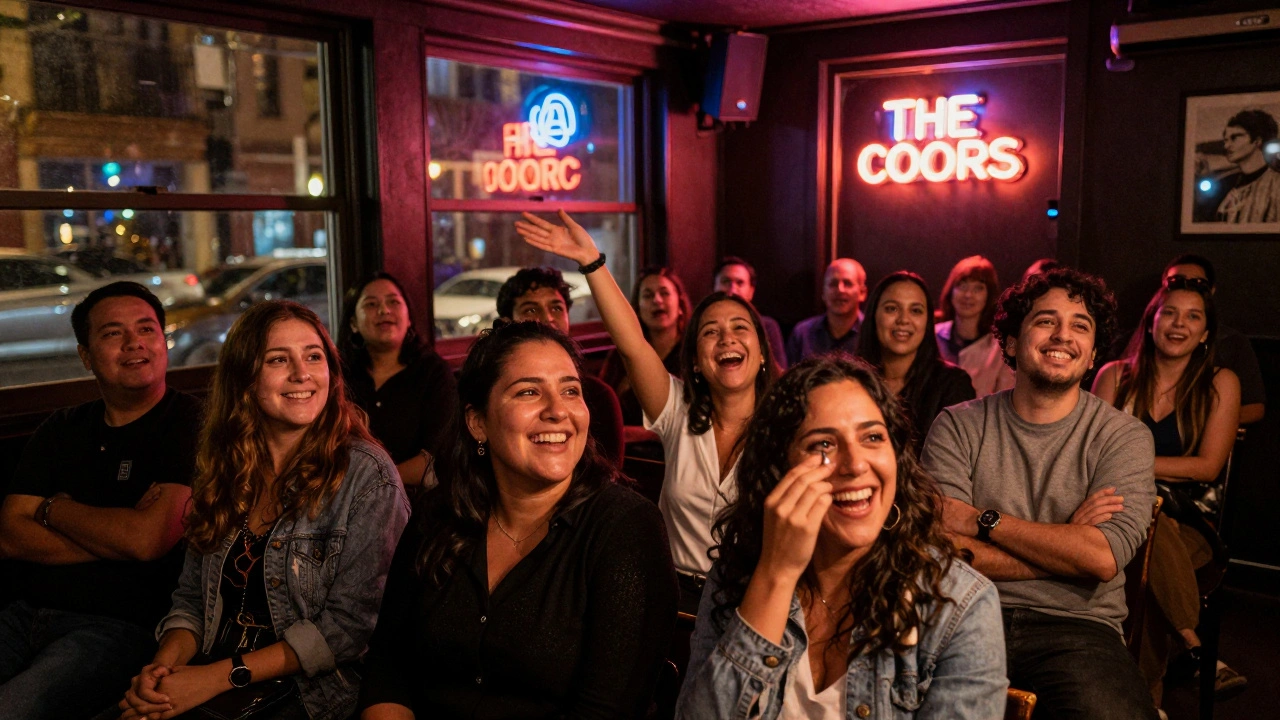 Audience members in Soho's Comedy Store laughing together under neon glow, one person wiping a tear from laughter during a stand-up set.